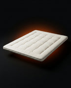 Cream white quilted floor mattress floating on a dark backdrop with orange glow
