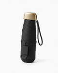 Compact black UV umbrella folded with gold capsule cap and wrist strap
