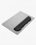 Black contoured memory foam wrist rest on a gray felt desk mat on white