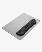 Black contoured memory foam wrist rest on a gray felt desk mat on white