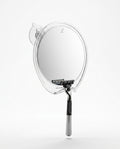 Round fog-free shower mirror with suction mount and razor hook holding a razor, studio shot