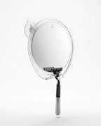 Round fog-free shower mirror with suction mount and razor hook holding a razor, studio shot