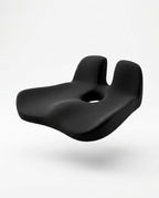 Black contoured memory foam seat cushion with coccyx cutout, floating on white