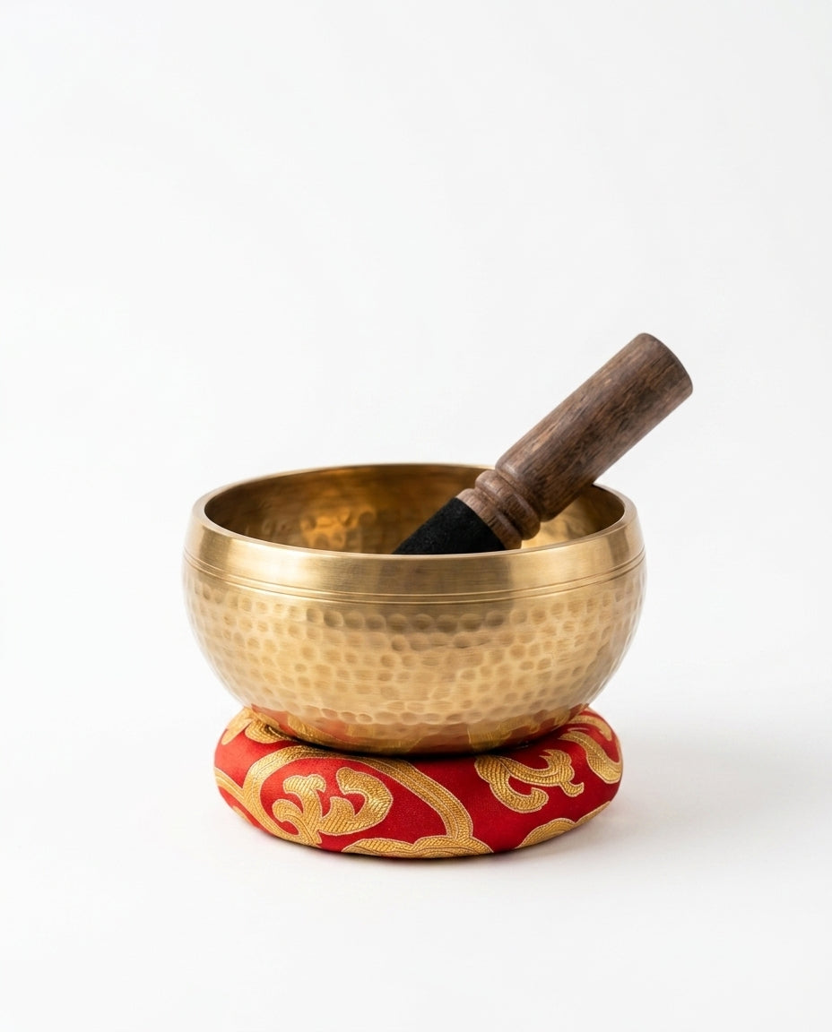 Hammered brass Tibetan singing bowl on a red cushion with wooden striker