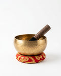 Hammered brass Tibetan singing bowl on a red cushion with wooden striker