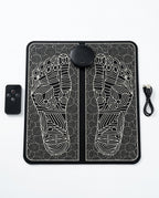 Black EMS foot massager mat with reflexology pattern, remote and USB cable on white