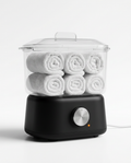 Mini towel warmer holding six rolled white towels under a clear lid