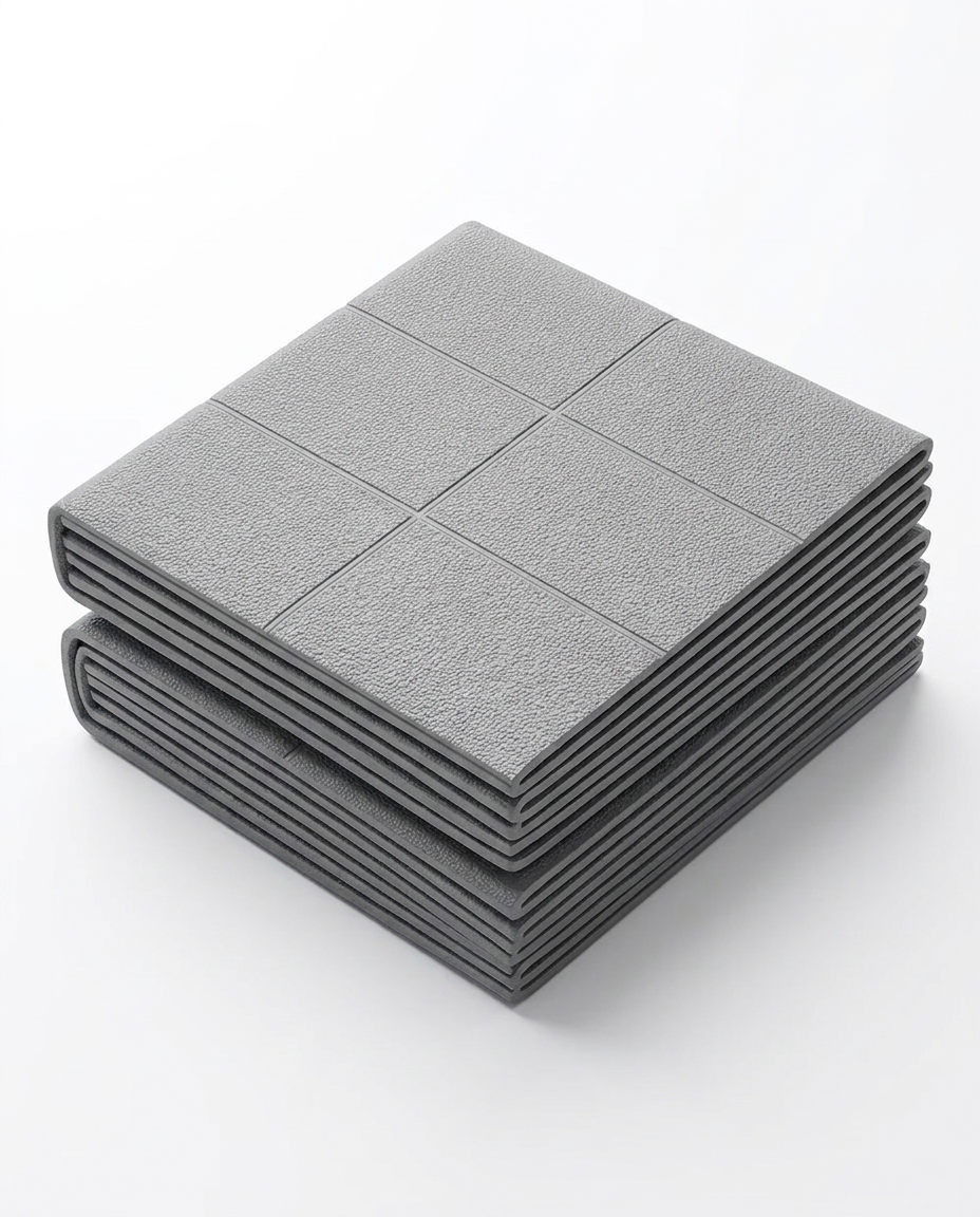 Grey foldable travel yoga mat folded into a compact square, studio shot
