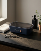 Ultrasonic cleaner on a dark bathroom vanity beside glasses and a ring