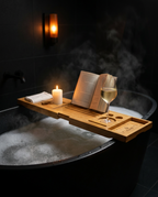 Bamboo caddy across a candlelit bathtub holding a book and wine glass
