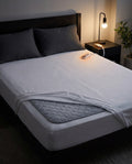 Quilted heated mattress pad on a bed with its controller on the nightstand at night