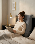 Woman reading in bed propped against the grey tufted backrest cushion