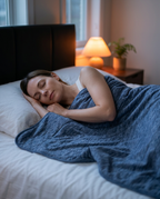Woman sleeping comfortably under the blue cooling blanket in a dim bedroom