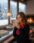 Woman in a snowy chalet wearing the red heated scarf by a fireplace
