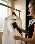 Woman steaming a white shirt on a hanger in a bright closet
