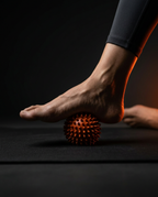 Bare foot rolling over orange spiky massage ball on a mat for plantar release