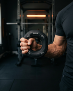 Man squeezing black resistance grip ring with flexed forearm in a gym