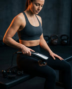 Woman using the handheld massager on her thigh in a gym recovery setting