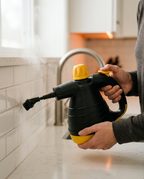 Hands aiming the steam cleaner at white subway tile grout in a kitchen