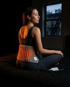 Woman seated on a bed with the heating pad wrapped around her lower back