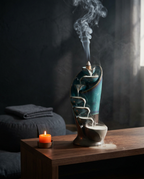 Waterfall incense burner cascading smoke in a dim meditation corner beside a candle
