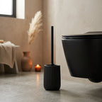 Black ribbed toilet brush holder beside a wall-hung toilet in a warm bathroom