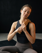 Woman in activewear rolling the wooden massage roller along her neck and shoulder