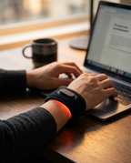 Red light wrist strap worn while typing on a laptop at a desk