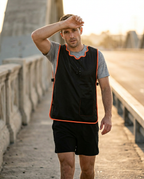 Runner on a bridge wiping sweat while wearing the black cooling vest at sunset