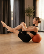 Woman doing Pilates core balance seated on orange mobility ball in bright room