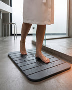 Bare feet stepping onto the grey stone bath mat after a shower
