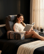 Woman reading a book in bed propped up against the gray bed rest pillow