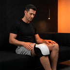 Man on a dark couch wearing the white heated knee massager on his knee