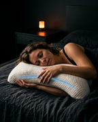 Woman sleeping on her side on the U-shaped cuddle pillow in a dim bedroom