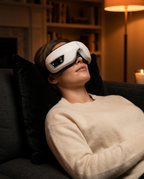 Woman reclining on a sofa wearing the eye massager in a cozy lamplit room