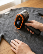 Hand using the fabric shaver to remove pills from a grey knit sweater