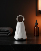 Cream face massage tool on black marble vanity beside serum bottle in warm light
