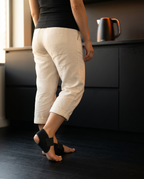 Person standing barefoot in a kitchen wearing the black heel cushions, rear view