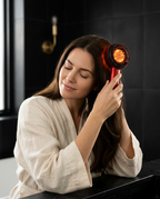 Woman in a robe using the glowing red scalp comb on her head in a bathroom