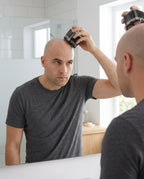 Bald man shaving his head with the 7D electric shaver at a bathroom mirror