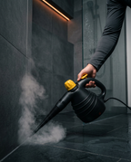 Person steam cleaning a dark tiled shower floor with rising steam