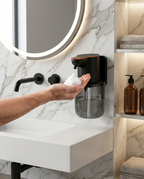 Wall-mounted soap dispenser releasing foam onto a hand in a marble bathroom