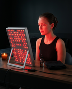 Woman seated at a desk facing the red light panel during a skincare session