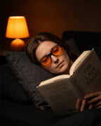 Woman reading a book in bed at night wearing orange-lens blue light glasses