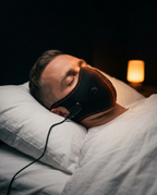 Man asleep in bed wearing the heated comfort mask, warm bedside lamp behind