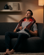 Man relaxing on a couch with the heated neck massager glowing red