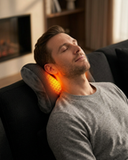 Man unwinding on a couch with the glowing heated neck pillow cradling his neck