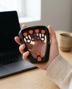 Hand using the finger trainer at a desk beside a laptop and coffee mug