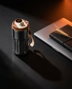 Smart temperature coffee mug on a dark desk beside a laptop and notebook