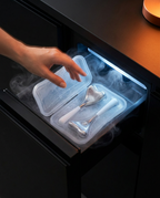 Hand pulling chilled steel eye massage tools from a frosty freezer drawer with cold mist